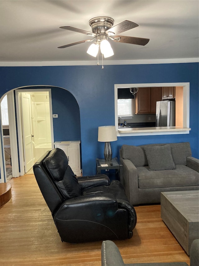 living room featuring light wood-style flooring, arched walkways, and ceiling fan