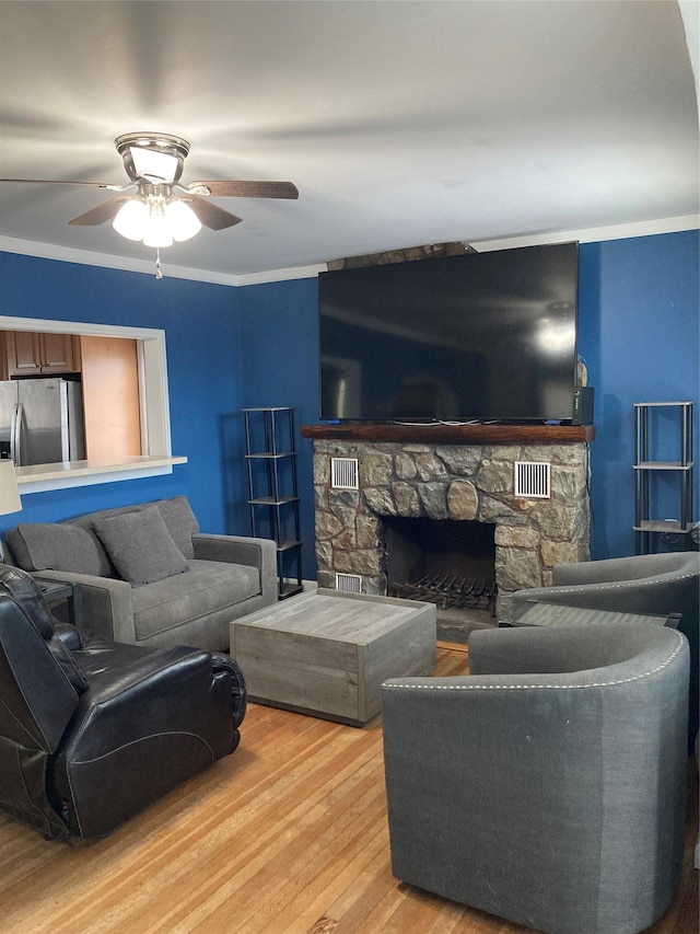 living room featuring ceiling fan, a stone fireplace, and light wood finished floors