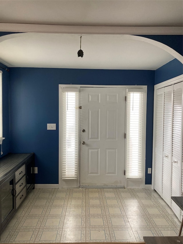 foyer featuring arched walkways, baseboards, and light floors