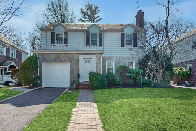 view of front of property featuring driveway, a balcony, stone siding, a chimney, and a front yard