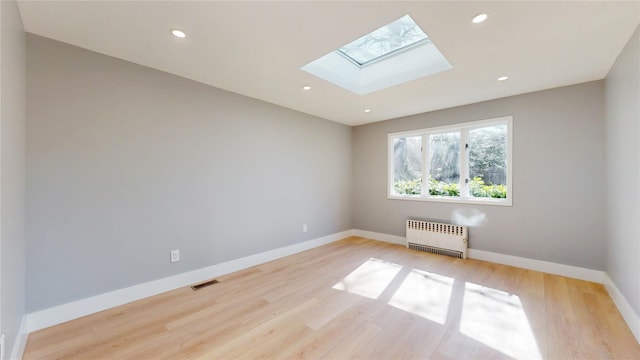 empty room with a skylight, visible vents, baseboards, radiator, and light wood-style flooring