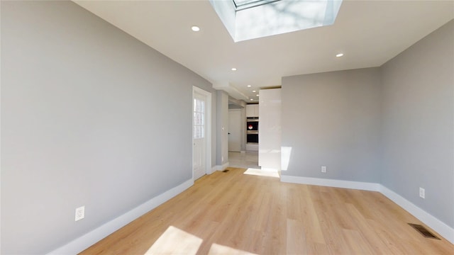 unfurnished living room featuring light wood-style flooring, a skylight, visible vents, and baseboards