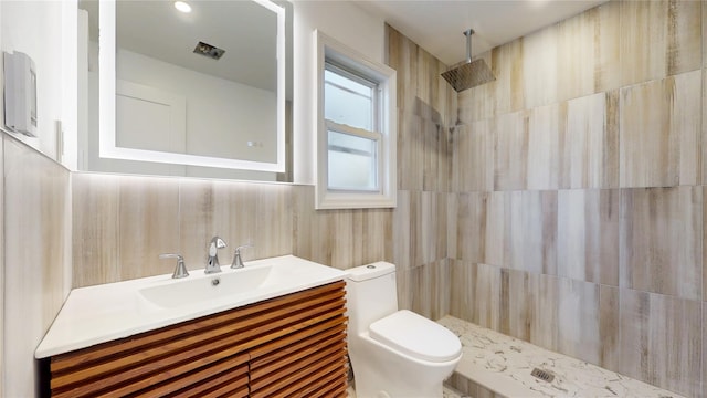 full bath with tile walls, tiled shower, vanity, and toilet