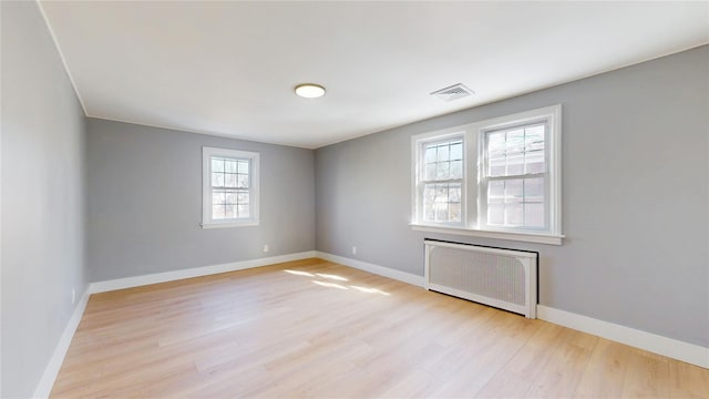 unfurnished room featuring light wood-style flooring, radiator heating unit, visible vents, and baseboards