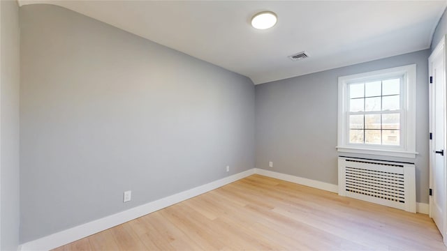 spare room featuring light wood finished floors, baseboards, visible vents, and radiator heating unit