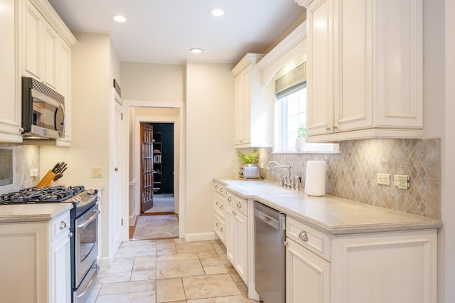 kitchen featuring tasteful backsplash, baseboards, appliances with stainless steel finishes, light countertops, and a sink