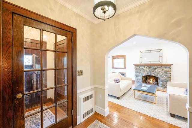 sitting room featuring arched walkways, crown molding, radiator, a stone fireplace, and hardwood / wood-style floors