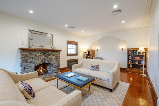 living room with ornamental molding, a stone fireplace, hardwood / wood-style flooring, and visible vents