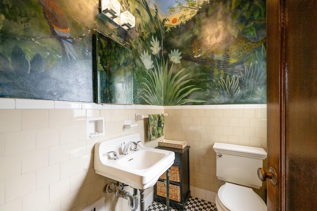 half bathroom featuring toilet, a wainscoted wall, and tile walls