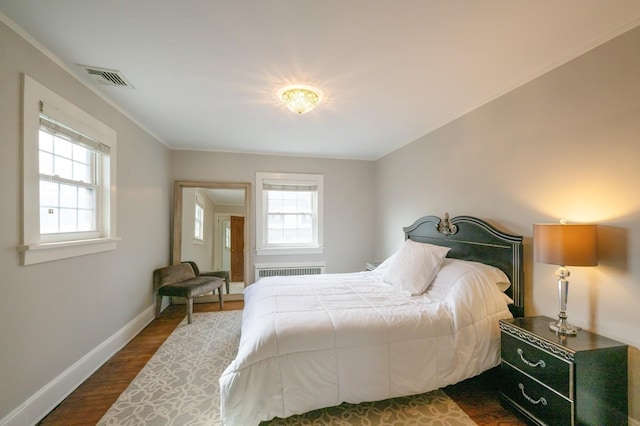 bedroom with radiator, dark wood-style floors, multiple windows, and visible vents