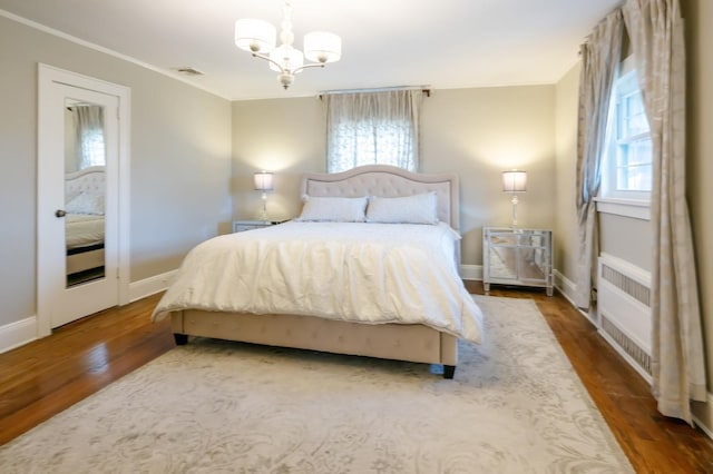 bedroom featuring a chandelier, wood finished floors, visible vents, baseboards, and crown molding