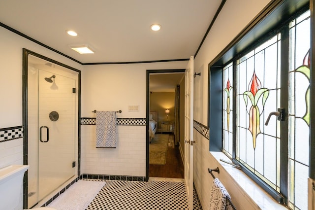 bathroom featuring recessed lighting, a wainscoted wall, tile walls, a shower stall, and ensuite bath