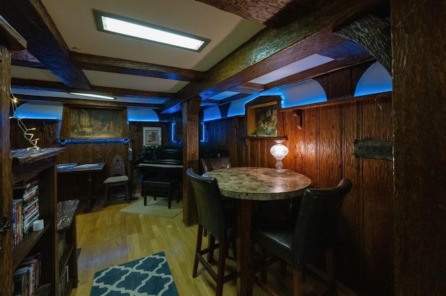 dining room featuring wood walls, beamed ceiling, and wood finished floors