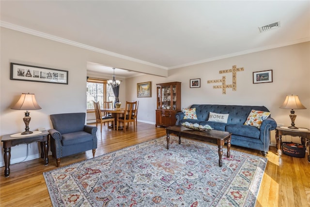 living area featuring baseboards, visible vents, wood finished floors, an inviting chandelier, and crown molding