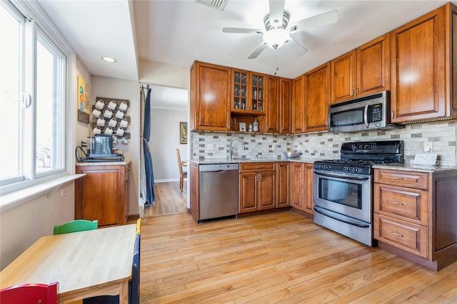 kitchen featuring appliances with stainless steel finishes, brown cabinets, backsplash, and light wood finished floors