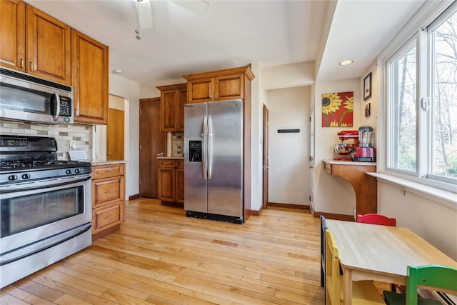 kitchen featuring stainless steel appliances, backsplash, brown cabinetry, light wood-style floors, and baseboards