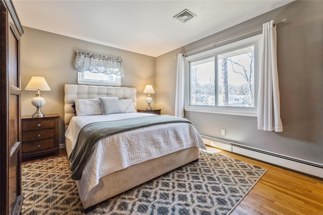 bedroom featuring multiple windows, visible vents, baseboard heating, and wood finished floors