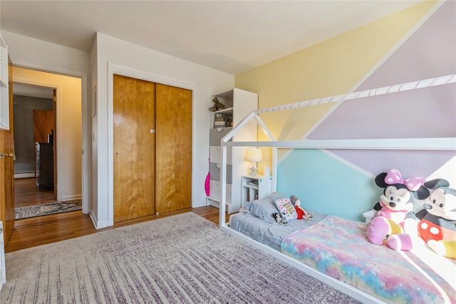 bedroom with baseboards, a closet, a baseboard heating unit, and wood finished floors