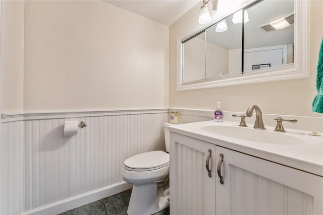 half bathroom featuring visible vents, toilet, a wainscoted wall, tile patterned floors, and vanity