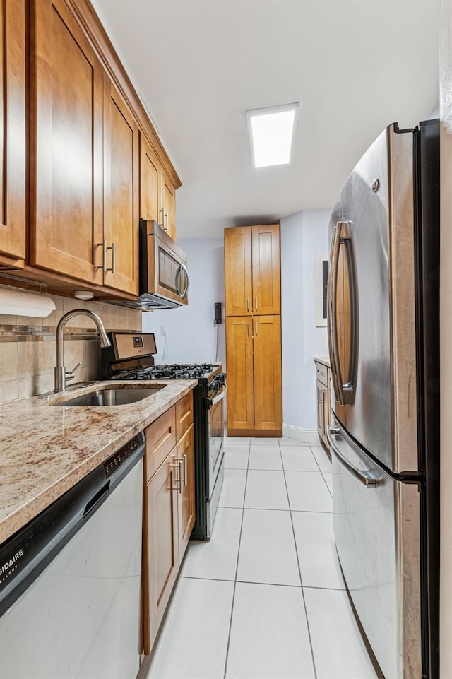 kitchen featuring light tile patterned floors, a sink, light stone countertops, stainless steel appliances, and backsplash