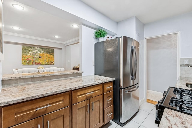 kitchen with light tile patterned floors, light stone counters, freestanding refrigerator, brown cabinets, and crown molding