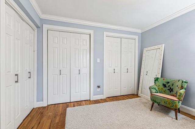 bedroom with crown molding, baseboards, wood finished floors, and multiple closets