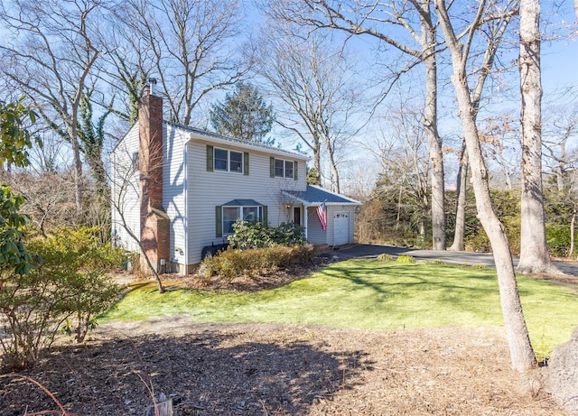 view of front of house with an attached garage, driveway, a chimney, and a front yard