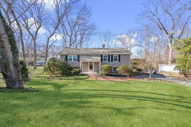 bi-level home with a chimney, fence, and a front yard