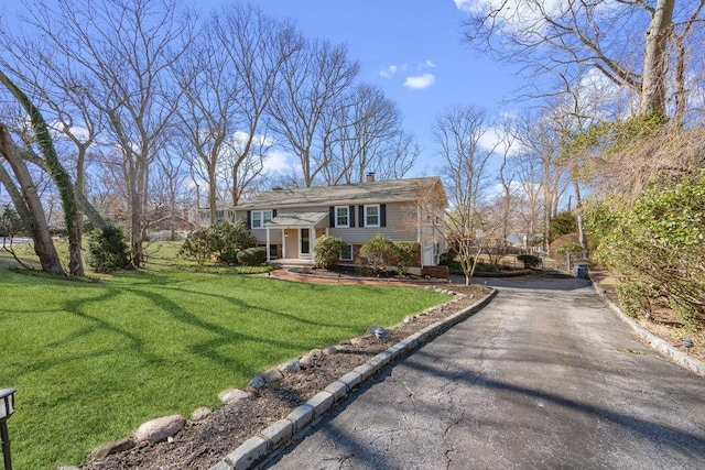 raised ranch featuring driveway, a chimney, and a front lawn