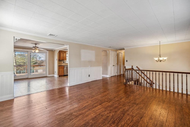 unfurnished room with ceiling fan with notable chandelier, wood finished floors, visible vents, ornamental molding, and wainscoting