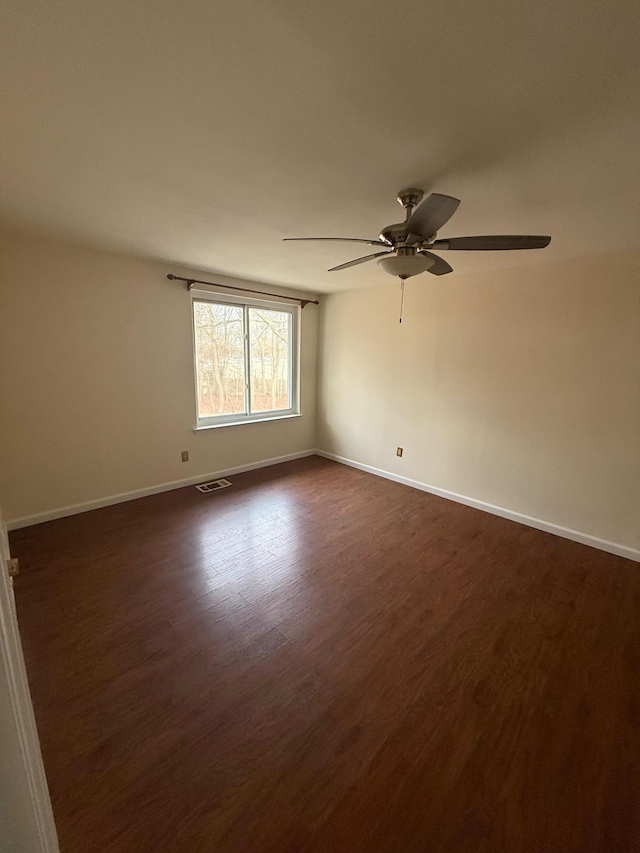 empty room featuring dark wood-style floors, visible vents, baseboards, and a ceiling fan