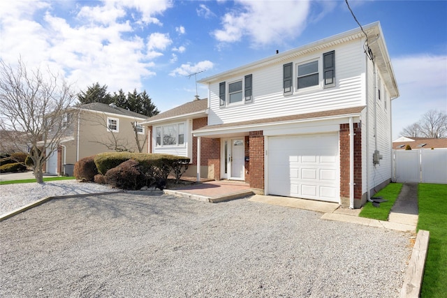 split level home with gravel driveway, an attached garage, fence, and brick siding