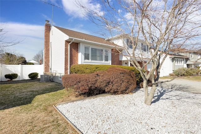 split level home with brick siding, a front lawn, fence, central air condition unit, and a chimney