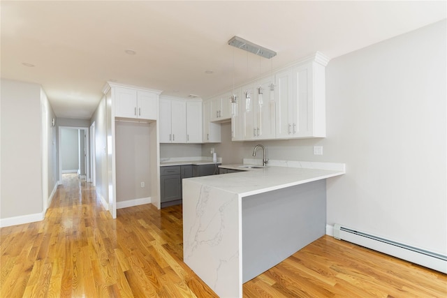 kitchen with a peninsula, light wood finished floors, a baseboard heating unit, and a sink