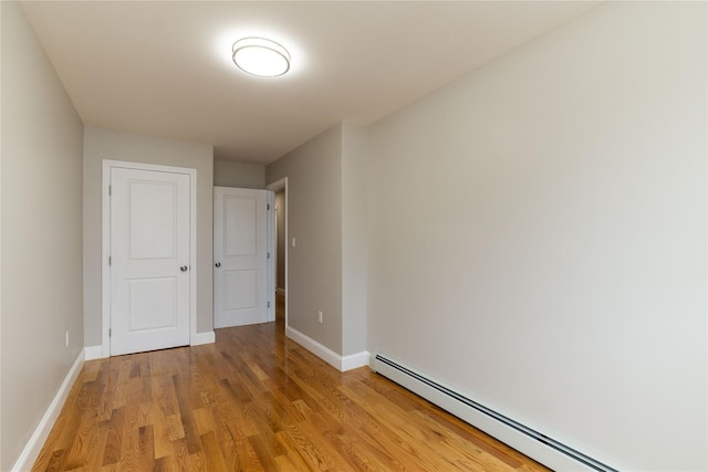 empty room with light wood finished floors, baseboards, and a baseboard heating unit