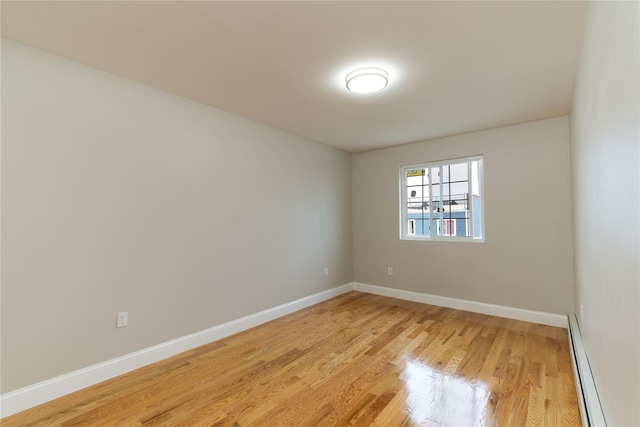 spare room with a baseboard heating unit, light wood-style flooring, and baseboards