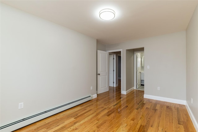 spare room with a baseboard heating unit, light wood finished floors, and baseboards