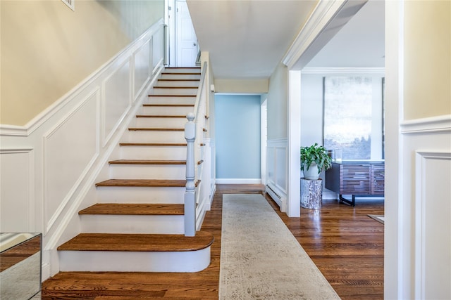 stairway featuring a wainscoted wall, baseboard heating, a decorative wall, and wood finished floors