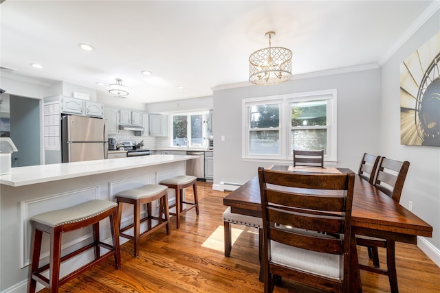 dining area featuring ornamental molding, a baseboard radiator, light wood-style flooring, and baseboards