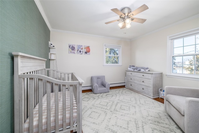 bedroom featuring a baseboard heating unit, ornamental molding, ceiling fan, wood finished floors, and a nursery area