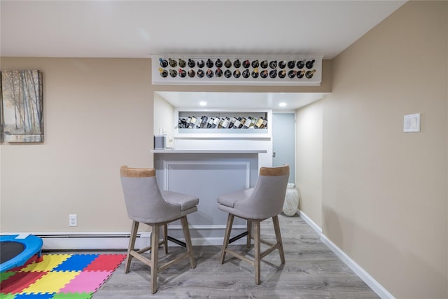 bar featuring a baseboard radiator, wood finished floors, and baseboards