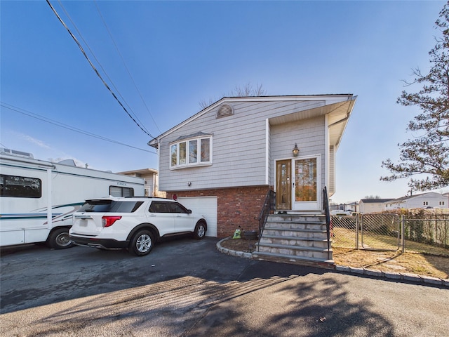 tri-level home with driveway, entry steps, a gate, fence, and brick siding