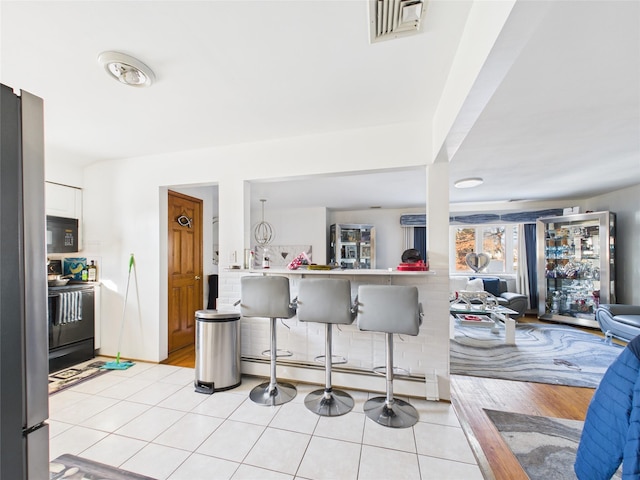 kitchen featuring light tile patterned floors, visible vents, white cabinetry, black appliances, and a kitchen bar