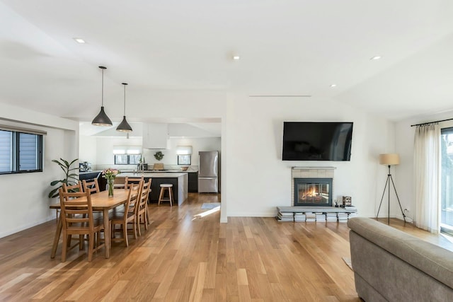 dining area featuring vaulted ceiling, a tiled fireplace, a wealth of natural light, and light wood-style floors