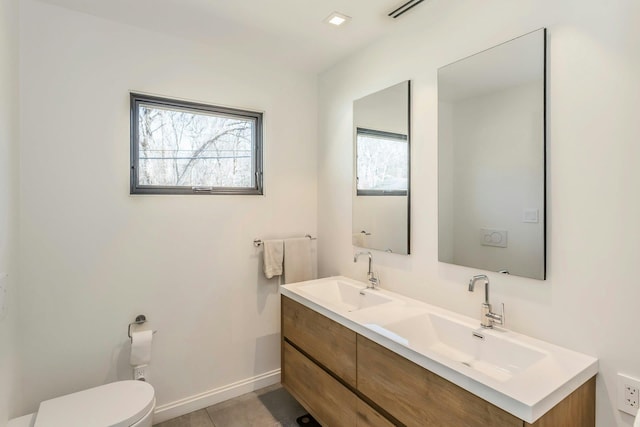 bathroom with double vanity, a sink, toilet, and baseboards