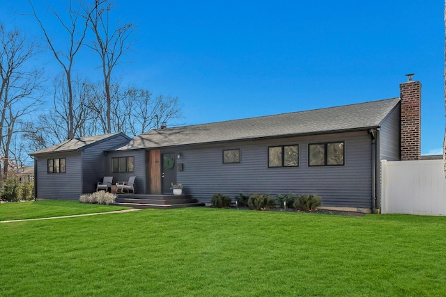 rear view of house featuring a lawn, a chimney, and fence