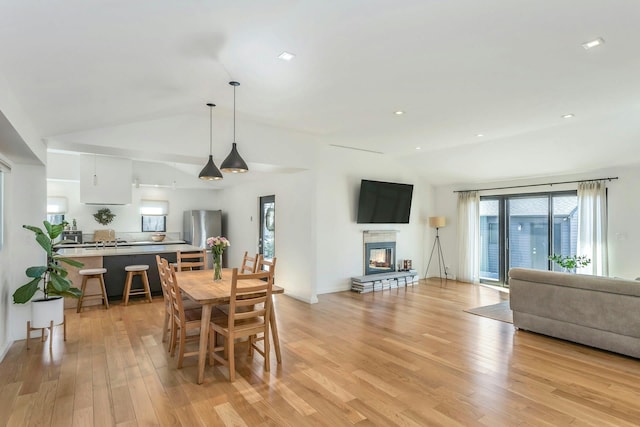 dining space featuring lofted ceiling, a glass covered fireplace, light wood finished floors, and recessed lighting