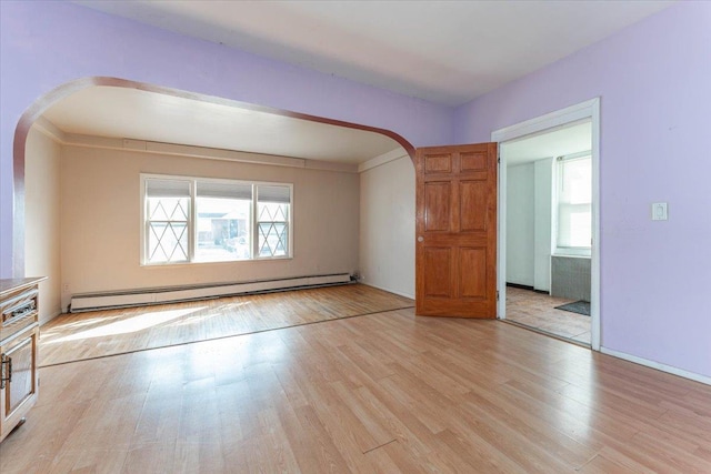 empty room featuring a baseboard heating unit, arched walkways, and light wood-style flooring