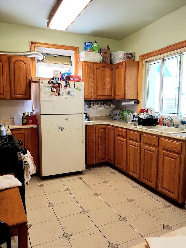 kitchen featuring light countertops, freestanding refrigerator, and brown cabinets