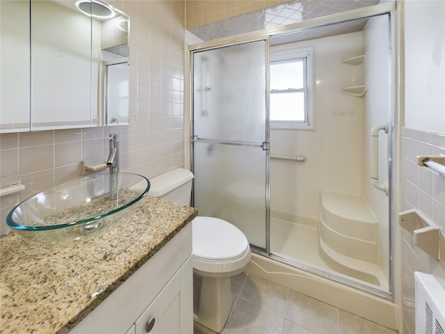 full bath featuring a stall shower, toilet, tile patterned flooring, vanity, and tile walls